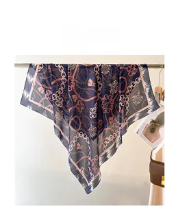 Detail of navy silk scarf with pink chain and floral patterns hanging near a bag