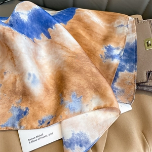 Detailed close-up of blue and yellow tie-dye silk scarf with premium rolled edges