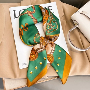 Elegante foulard in seta con stampa a catena verde e arancione su un trench beige chic