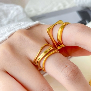 Detail of layered wavy gold rings and geometric bands on a knit sweater cuff