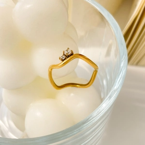 Macro detail of 18K gold-plated wavy ring with dual cubic zirconia on cream background