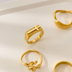 Detailed view of 18K gold plated titanium rings with cross and leaf motifs on display