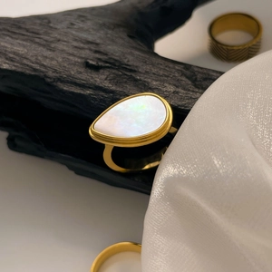 Detail view of 18K gold plated ring with iridescent teardrop shell on charred wood