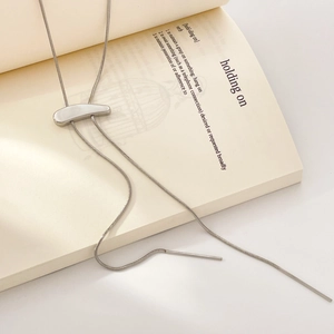 Close-up of a silver bolo tie necklace with sleek curved slider on a book page