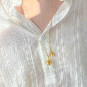 Detail view of double teardrop necklaces in 18K gold plated steel on a striped shirt