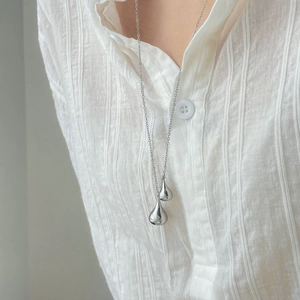 Close-up of dual silver teardrop pendants on an O-chain worn on a white linen shirt