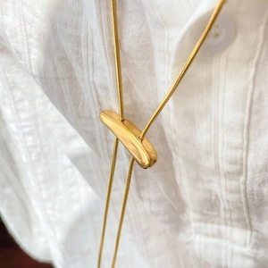 Detail of adjustable gold slider on snake chain necklace worn over white shirt