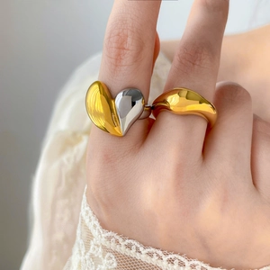 Gros plan d'une bague cœur bicolore et d'une bague dorée fluide sur main avec dentelle