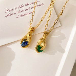 Close-up of vintage textured gold hand pendants holding blue and green pear-cut zircons