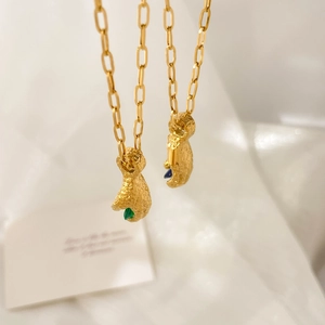 Close-up of 18K gold-plated fist pendants holding green and blue teardrop zircon gems