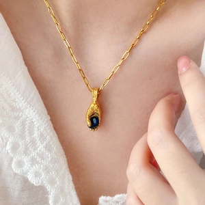 Detail of hand-shaped pendant holding a blue gemstone on an 18K gold plated snake chain