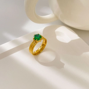Détail macro d'une bague dorée multi-rangs avec un zircon vert serti à six griffes