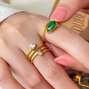 Gros plan de bagues multicouches dorées 18K avec zircone verte et en forme de coeur