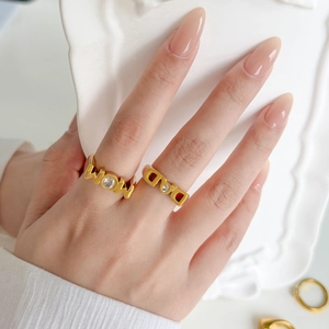 Close-up of gold MOM ring with cubic zirconia worn by hand on a white ceramic plate
