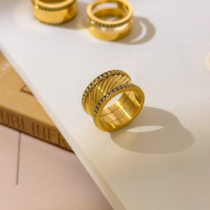 Gros plan d'une bague large plaquée or avec texture torsadée et double rangée de zircons