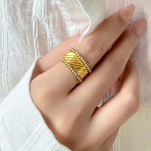 Gros plan sur une bague large plaqué or 18K avec texture torsadée et rangées de zircons