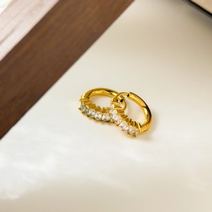 Macro shot of gold plated hoop earrings with baguette-cut zircon stones on stone base