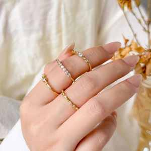 Close-up of four thin 18K gold-plated rings with micro-set diamonds on white fabric