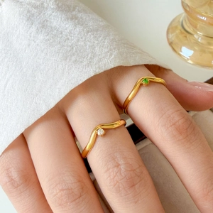 Detail of stacked V-shaped gold rings with clear and green crystals on hand