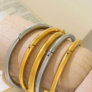 Polished gold and silver minimalist bangle bracelets on a wooden display stand