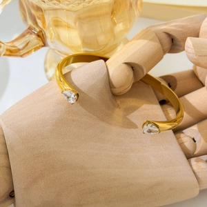 Close-up of golden C-shaped open bangle with pear-cut zircon on a wooden mannequin hand