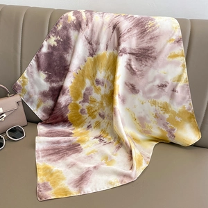 Artistic tie-dye silk scarf with purple and yellow gradient draped on a leather sofa
