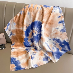 Detail of gradient tie-dye silk scarf draped on a leather chair with stylish accessories