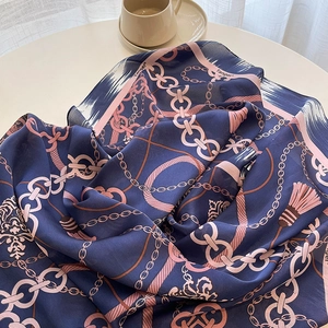 Blue and pink silk scarf with chain print and tassels on a minimalist table
