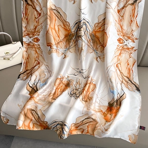 Artistic ink-wash print silk shawl in warm orange and beige on a grey leather sofa