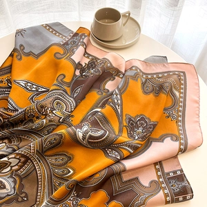 Détail d'un foulard en soie à motifs cachemire drapé sur une table blanche sous la lumière