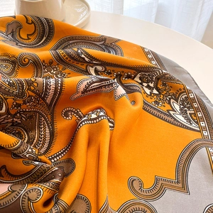 Détail d'un foulard en soie orange à motif cachemire posé près d'une tasse blanche