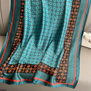 Elegant silk-like scarf with green geometric grid and orange floral print on a sofa