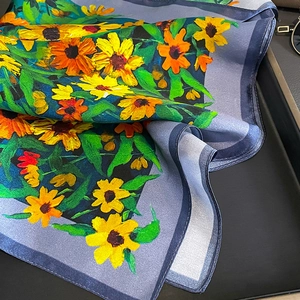Elegant silk scarf featuring vibrant sunflower and daisy floral patterns on deep blue fabric