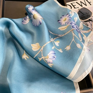 Foulard in seta celeste con stampe di margherite e bordi crema su un vassoio chic