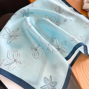 Floral silk scarf with white magnolia print and deep blue border on a wooden background
