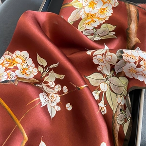 Detail view of red-brown silk scarf with white plum blossom print and satin texture