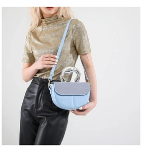Macro detail of a light blue saddle bag with silver metal handle and textured flap fabric