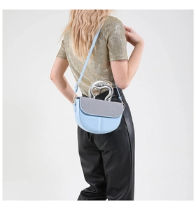 Detail of light blue crossbody saddle bag with unique silver metallic handle worn by model