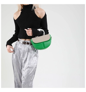 Detail of green leather saddle bag with woven flap and curved silver metal handle