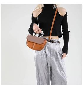 Detailed shot of brown leather bag with woven texture flap and round silver metal handle