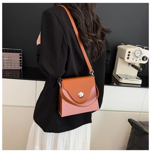 Détail du sac boîte rose avec rabat en cuir marron porté par un mannequin en costume