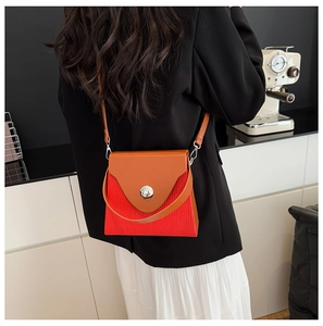 Détail du sac bandoulière bicolore à plis rouges et cuir orange porté par un mannequin