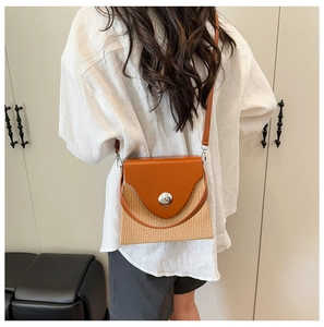 Détail d'un sac bandoulière en cuir marron et paille avec une grande boucle en métal argenté
