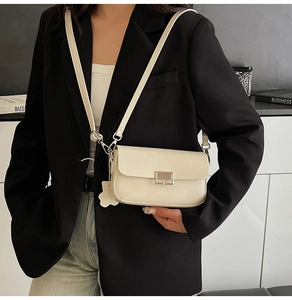 Close-up of a cream leather crossbody bag with a silver metal clasp on a black blazer