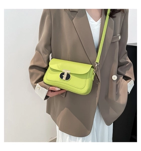 Modèle portant un sac bandoulière en cuir vert fluo avec boucle T dorée et blazer marron