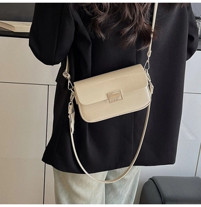 Detail of cream flap crossbody bag with gold metal buckle worn over a black blazer