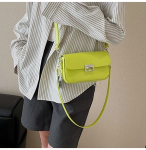 Green leather flap crossbody bag with silver buckle worn by a model in casual attire