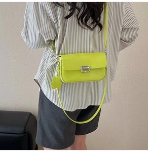 Neon green square crossbody bag with silver buckle and bear charm on striped shirt
