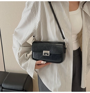 Detail of a black crossbody bag with silver buckle worn over a striped shirt