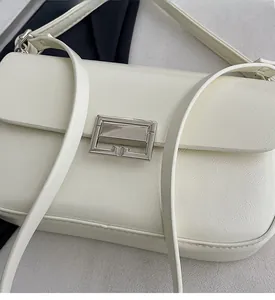 Detail shot of ivory leather texture and silver rectangular buckle on this square handbag